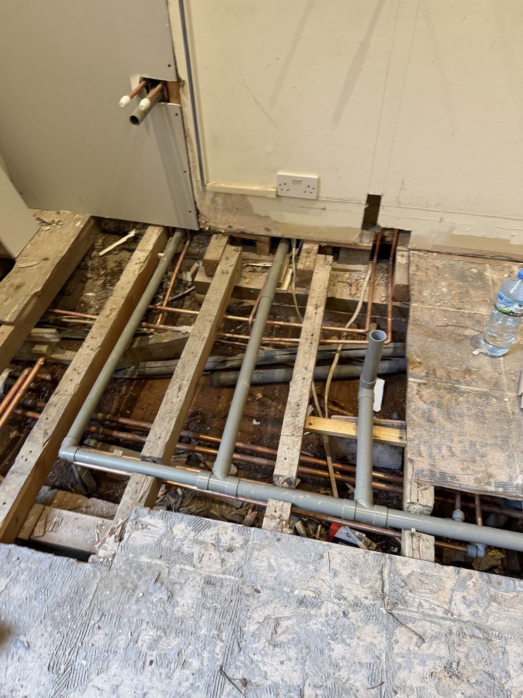 Floorboards lifted showing copper and waste pipe runs between joists